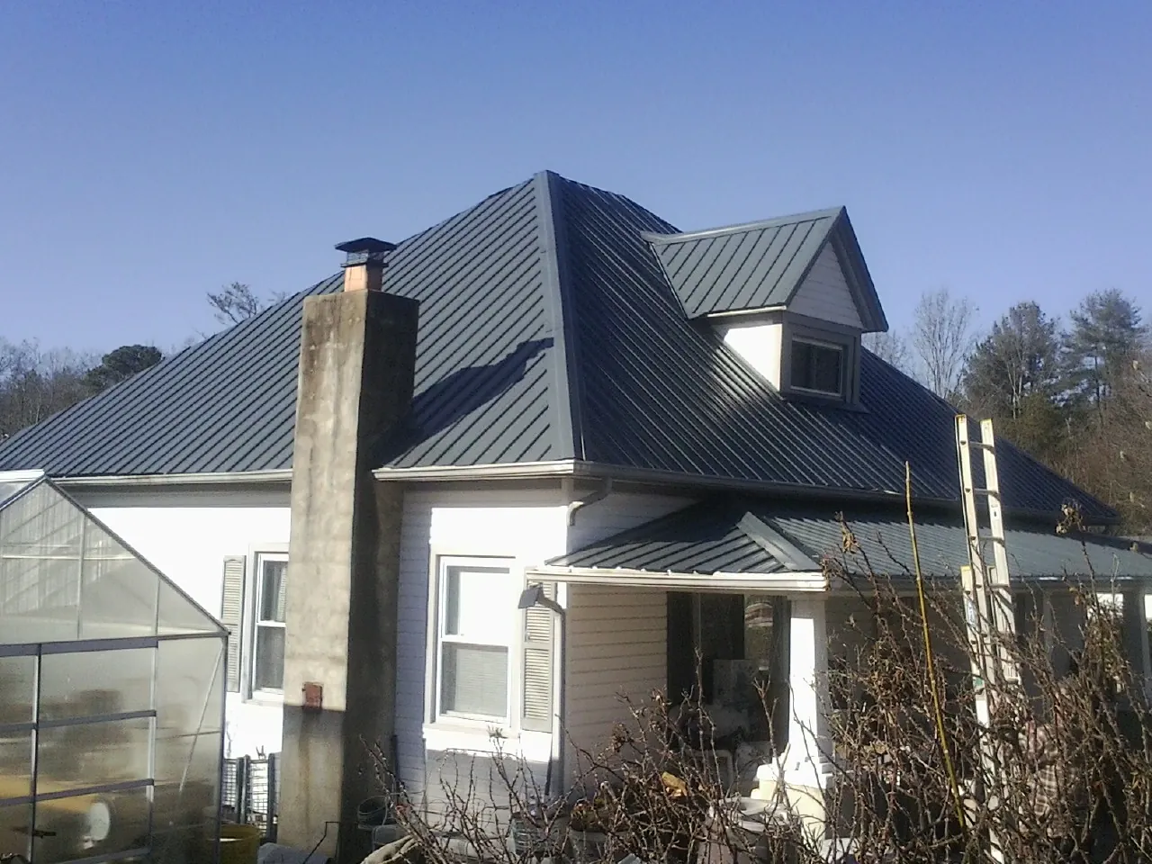 Dark blue standing seam metal roof on a white farmhouse with dormer — Slate & Tile Roof Repair by Roofing Brothers in Valley Park