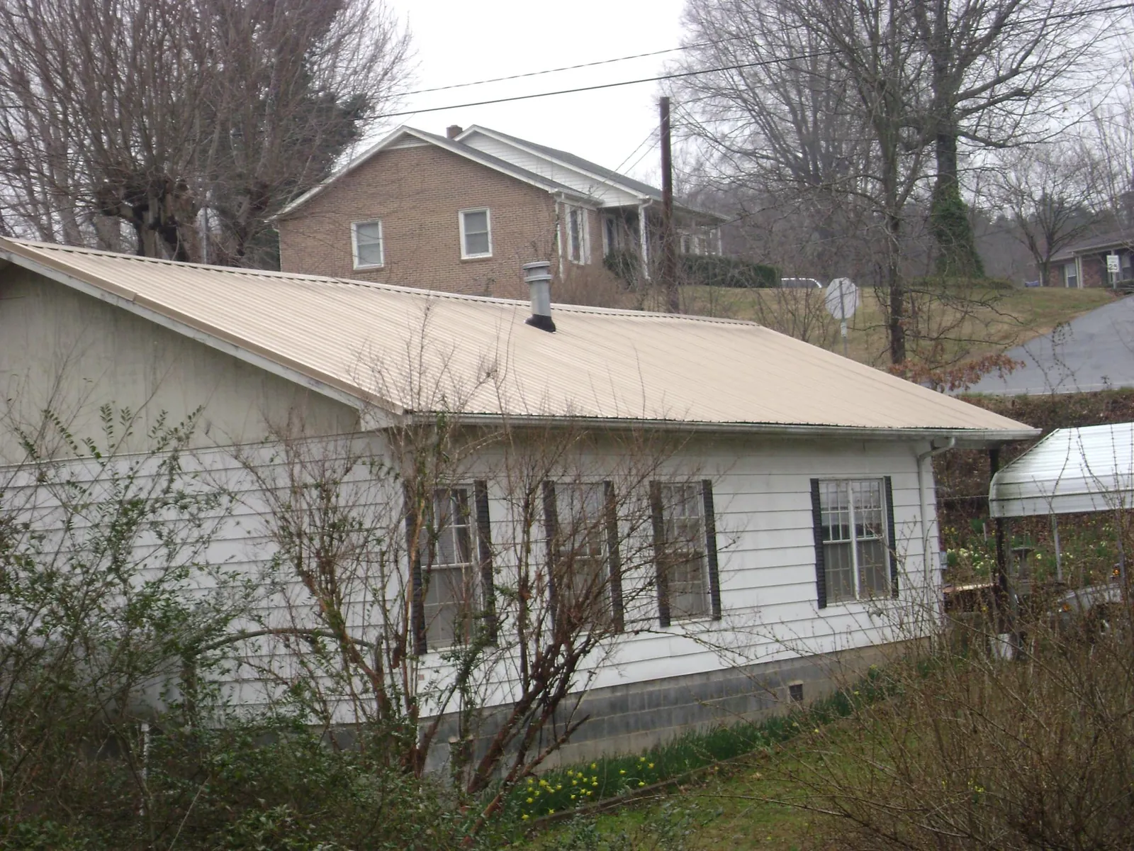 Tan metal roof on a white sided house set into a hillside — Commercial Roofing by Roofing Brothers in Valley Park