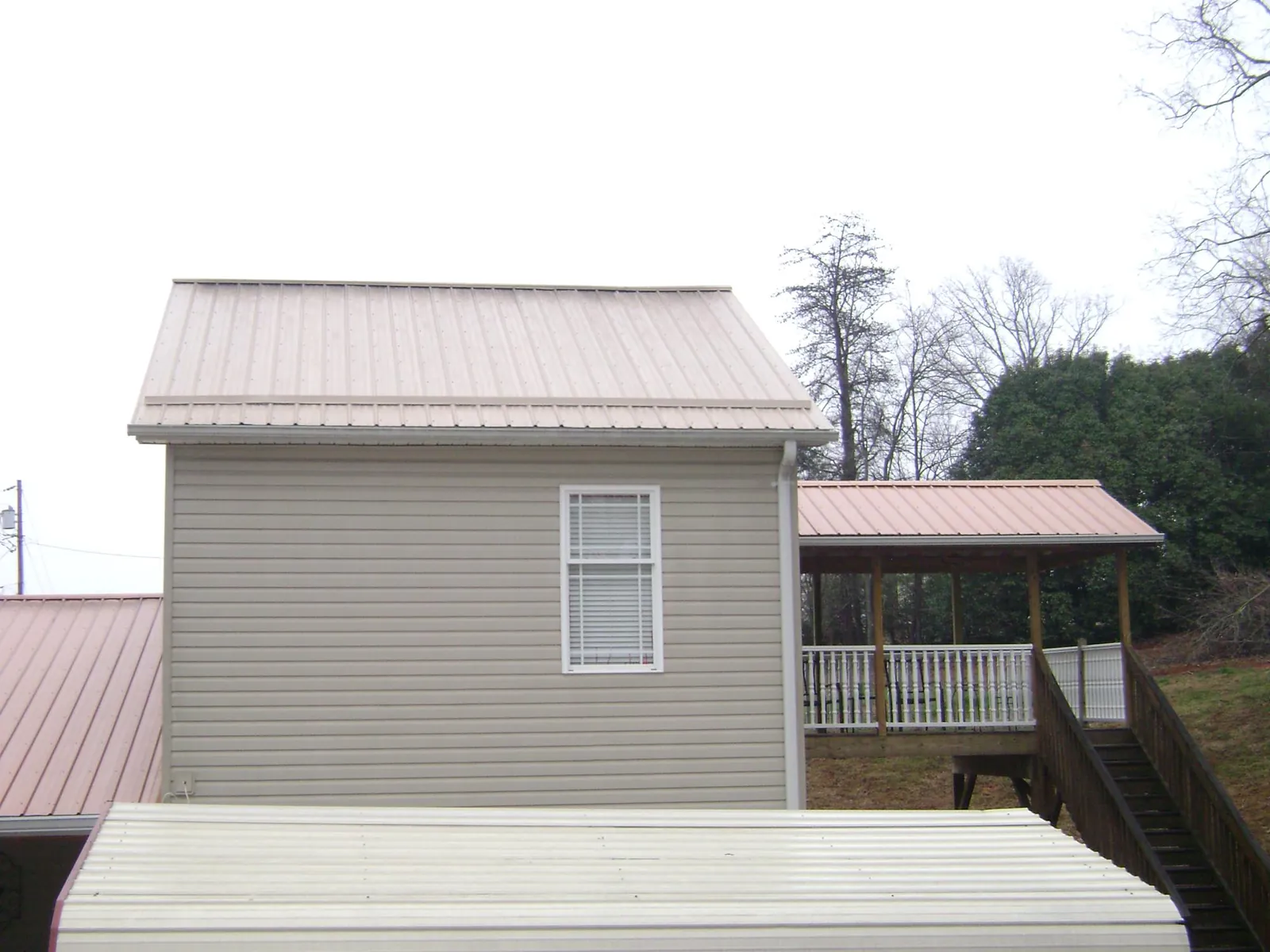 Tan metal roofs on a two story addition and attached porch, from a Roof Replacement job in Valley Park